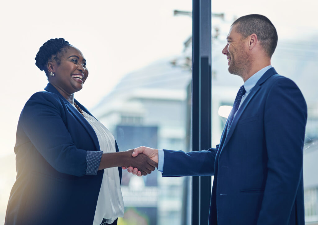 Two business professionals smiling and shaking hands, representing a positive professional relationship.